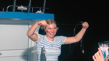 A person standing on a boat deck with a railing and a blue container in the background.