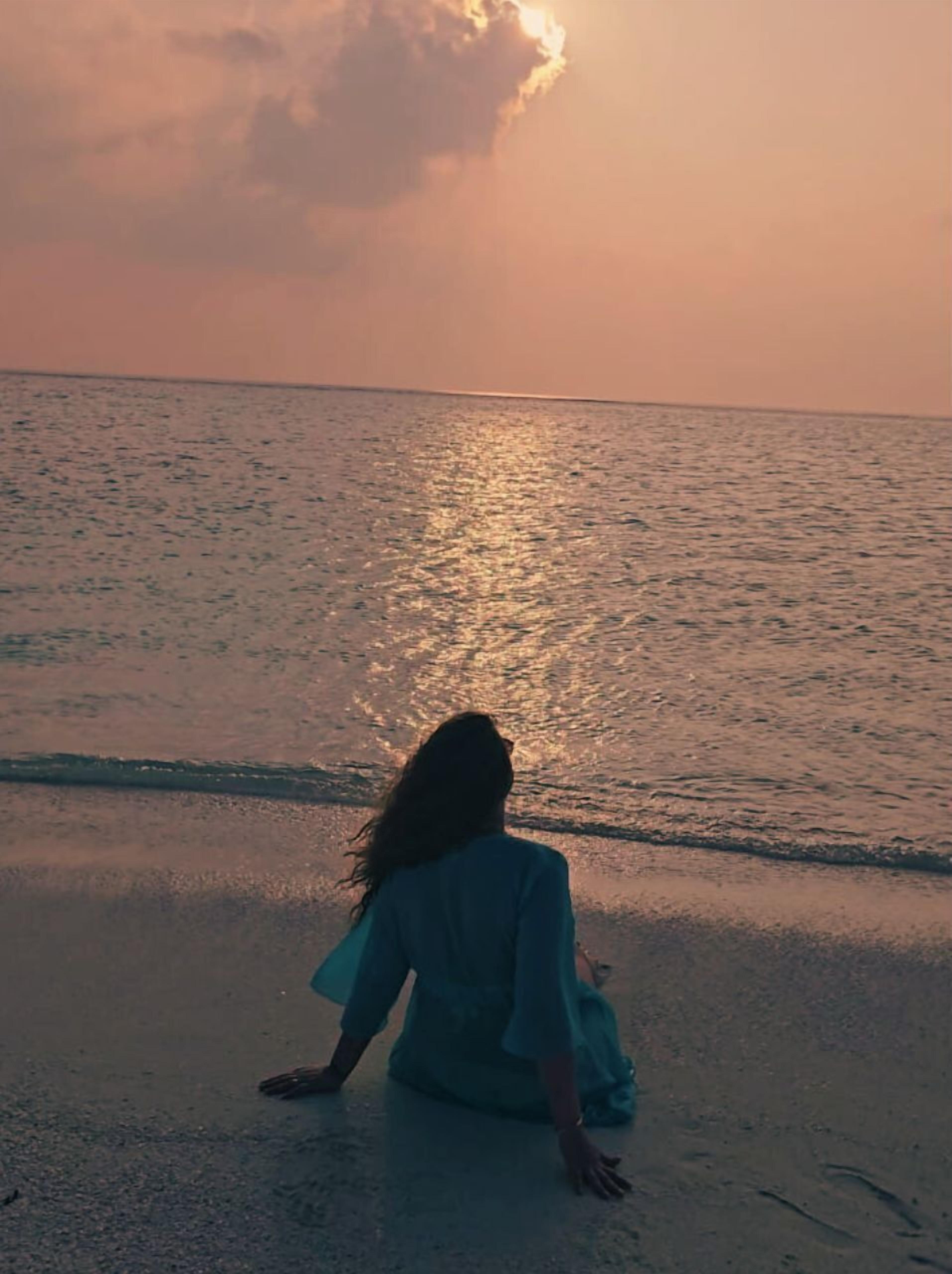 A person sitting on the beach facing the ocean at sunset.
