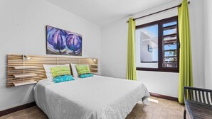 Une chambre à coucher avec un lit, une tête de lit, une fenêtre avec des rideaux et un tableau accroché au mur.