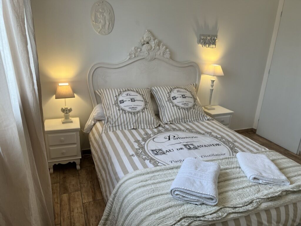 A neatly made bed with striped bedding and pillows, two bedside lamps, and a decorative wall piece.