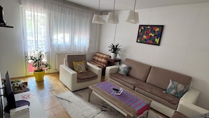A modern living room with a sofa, armchairs, a coffee table, a TV, and a potted plant. - SunnyHill Apartments (Pristina)