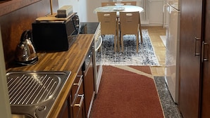 A compact kitchen with wooden cabinets, a built-in stove, and a dining area with a table and chairs. - SunnyHill Apartments (Pristina)