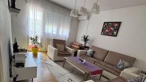 A modern living room with a sofa set, a coffee table, a TV, and a potted plant. - SunnyHill Apartments (Pristina)