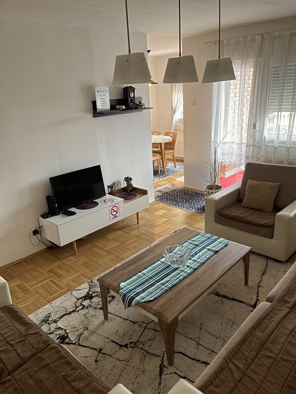 Un salon moderne doté d’un téléviseur à écran plat, d’une console blanche, d’un canapé, d’une table basse et de luminaires suspendus.