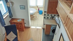 Une cuisine compacte équipée d’un lave-linge, un coin repas avec une table et des chaises, et un petit coin salon avec un fauteuil et une commode en bois.