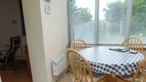 Un coin repas avec une table ronde recouverte d’une nappe à carreaux, entourée de chaises en bois.