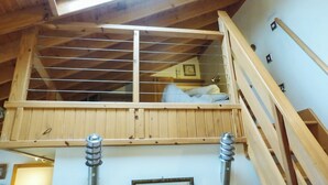 Une chambre en mezzanine avec un puits de lumière, des poutres en bois et une vue sur la pièce située en dessous.