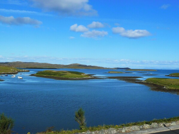 Een kustlandschap met kalm water, grasvelden en heuvels in de verte.