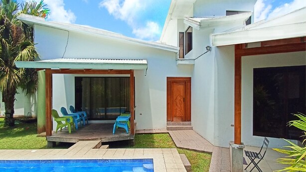 A modern house with a swimming pool, a covered patio with chairs, and a large wooden door.