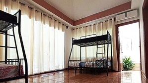 Una habitación con dos literas, suelo de baldosas, una ventana con cortinas y un equipo de aire acondicionado.