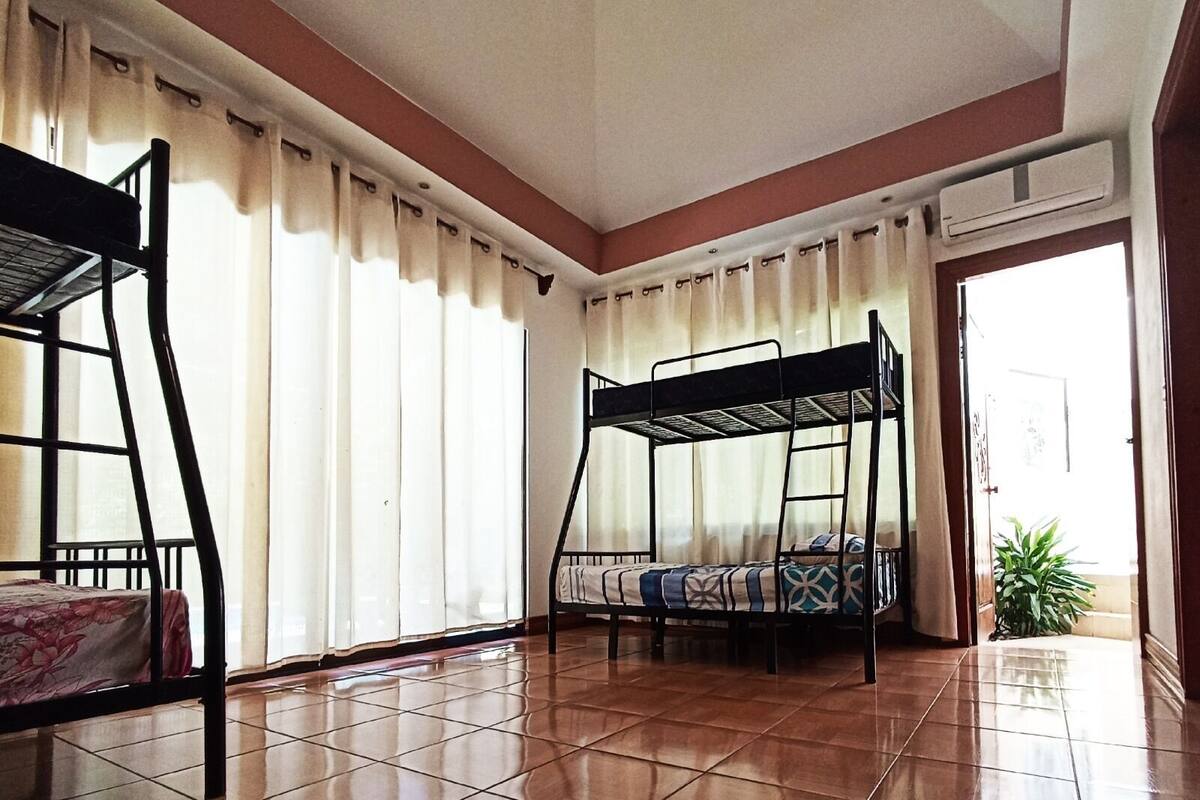 A room with two bunk beds, a tiled floor, a window with curtains, and an air conditioning unit.