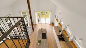 Un intérieur moderne avec un plancher en bois, un îlot central et une vue sur un jardin grâce à de grandes fenêtres.