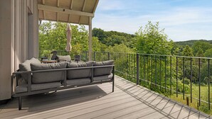 Une terrasse en bois avec un canapé gris et une table, donnant sur un paysage verdoyant et luxuriant.