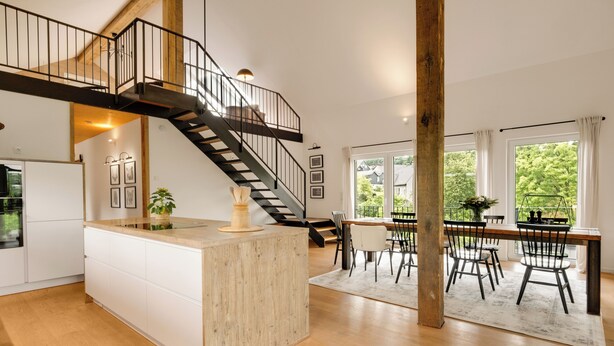 Une cuisine spacieuse dotée d’un îlot central, un coin repas avec une table et des chaises en bois, et un escalier menant à l’étage supérieur.