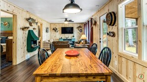 A wooden-paneled room with a dining table, chairs, a ceiling fan, and a mounted television. - Lured Den - Private Lakefront Cottage - HOT TUB! (Conover)