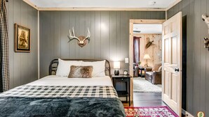 A bedroom with a bed, a mounted deer head, a framed picture, a nightstand, a lamp, and a door leading to another room. - Lured Den - Private Lakefront Cottage - HOT TUB! (Conover)