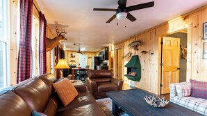 A cozy cabin interior with a leather sofa, a wooden dining table, and a ceiling fan. - Lured Den - Private Lakefront Cottage - HOT TUB! (Conover)