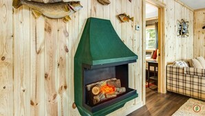A wooden interior with a fireplace, fish mounted on the wall, and a plaid sofa. - Lured Den - Private Lakefront Cottage - HOT TUB! (Conover)