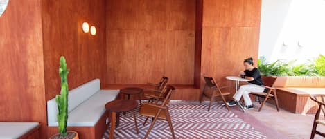 A modern outdoor seating area with wooden furniture, a cactus plant, and a patterned floor.