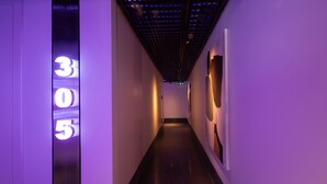 Un pasillo con números iluminados '305' que señalan los números de las habitaciones, un techo con diseño de cuadrícula y un piso pulido.