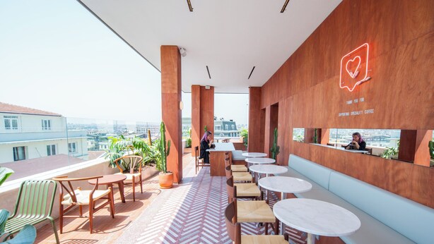 Un moderno café en la azotea con mobiliario de madera, suelo con patrón de espiga y vista a la ciudad.