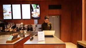 Mostrador de una cafetería con un ordenador portátil, equipo para preparar café y una pizarra de menú.