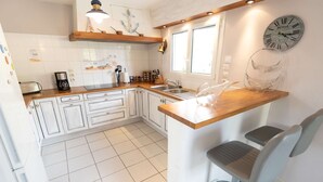 A kitchen with white cabinets, a wooden countertop, a sink, a bicycle clock, and a window. - Villa with heated pool & garden - 5 min from the sea, by Groom (Guidel)