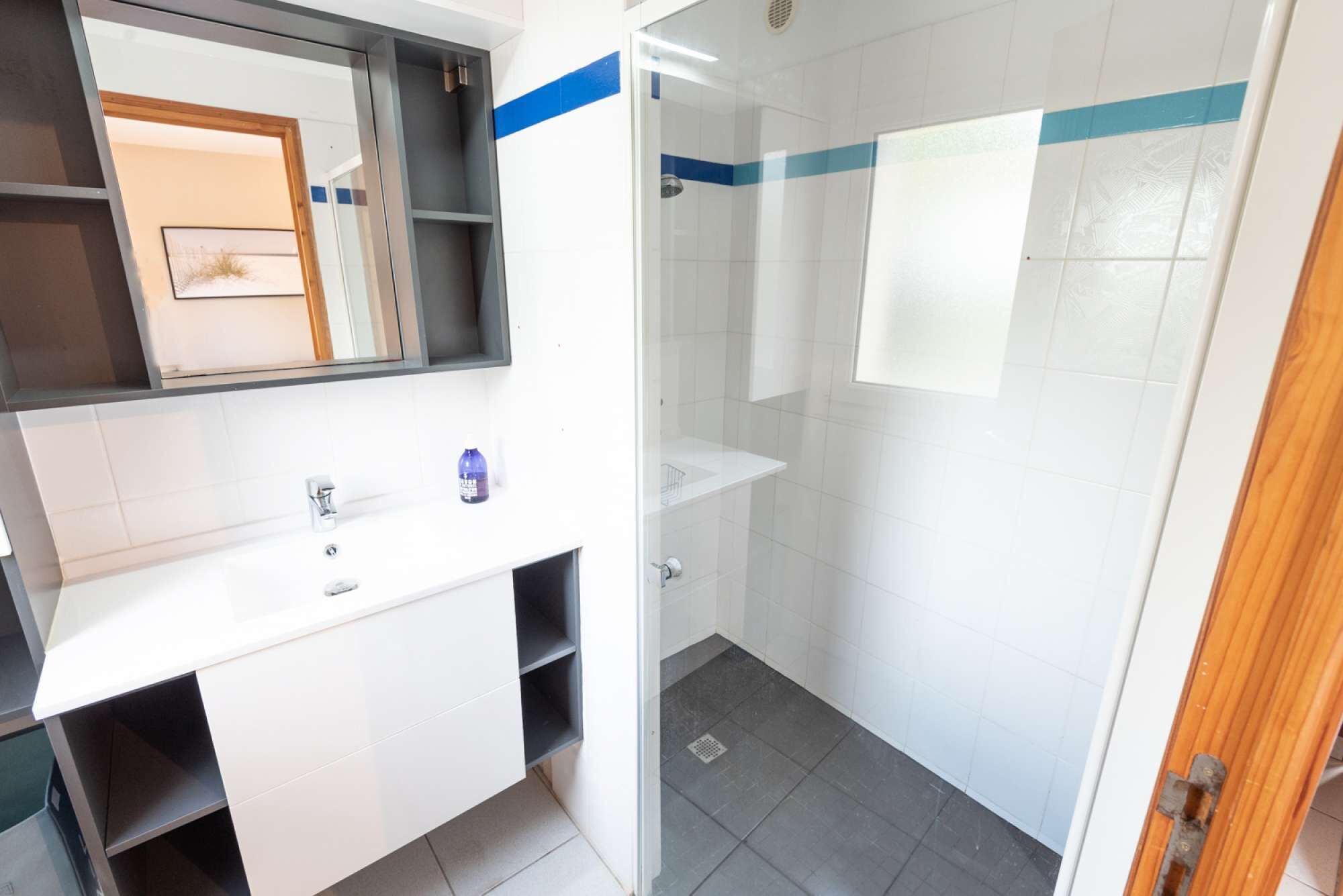 A modern bathroom with a glass shower enclosure, white tiles, and a blue stripe on the walls.