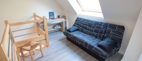 Ein Zimmer mit Etagenbett, einer Schlafcouch, einem Schreibtisch und einem Dachfenster.