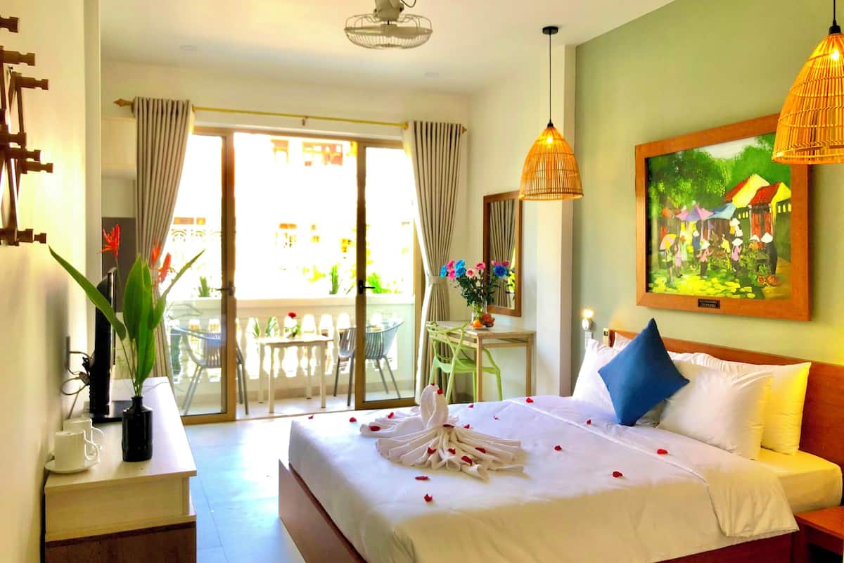 Habitación de hotel con una cama, un escritorio, una silla, una mesa, una planta en maceta y un cuadro en la pared.