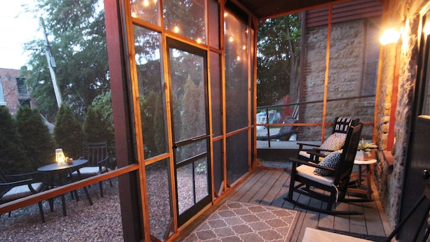 A covered outdoor seating area with tables and chairs, large windows, and a stone wall. - The Owl House, 1850's Historic Home: Luxury Steps from Downtown  (Galena)