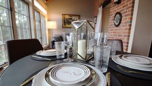 A dining table set with plates, glasses, and cutlery, featuring a candle and a decorative glass centerpiece. - The Owl House, 1850's Historic Home: Luxury Steps from Downtown  (Galena)