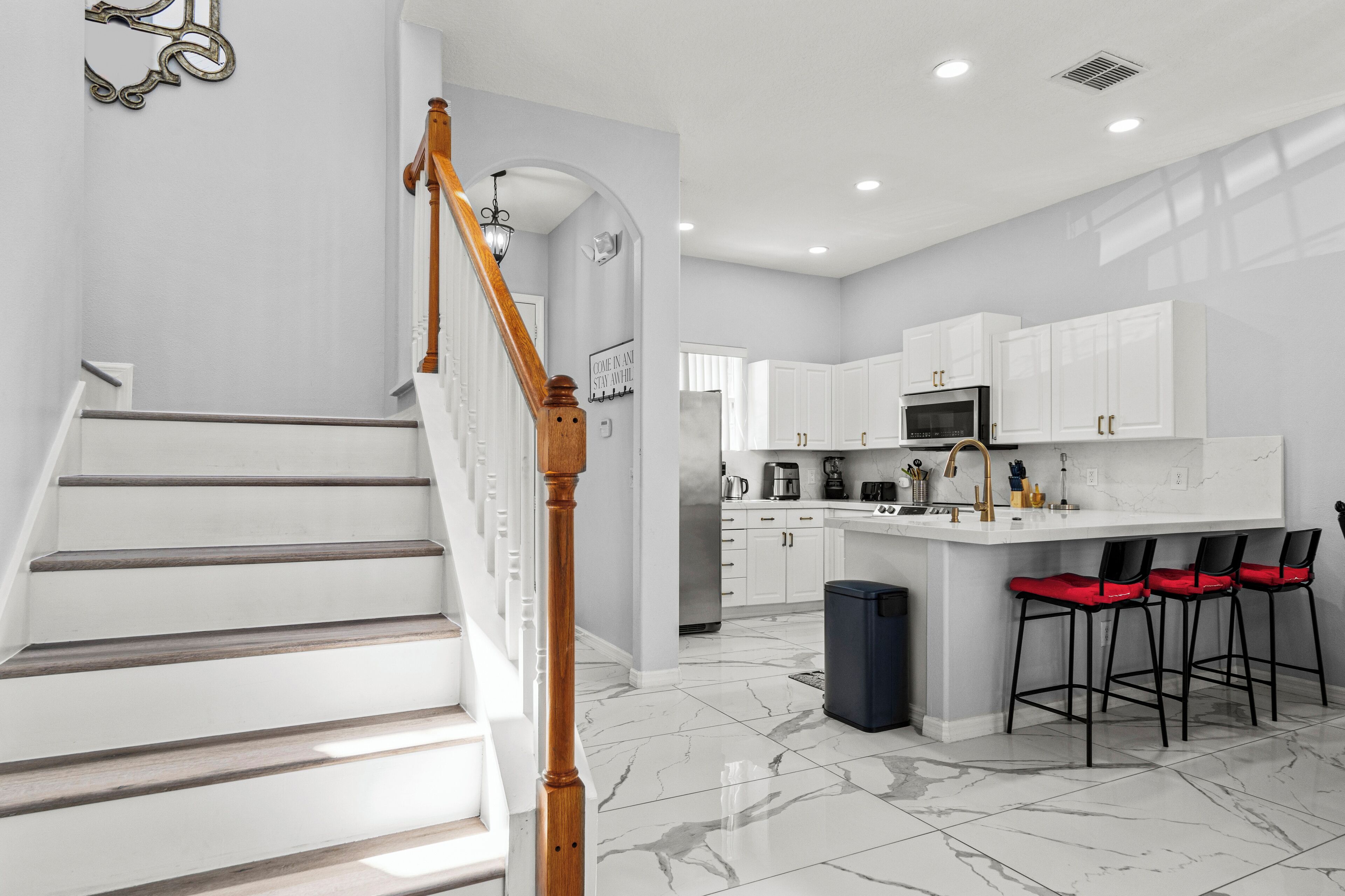 A modern kitchen with white cabinets, a marble floor, and a central island with red bar stools.