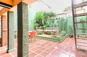 A patio area with a tiled floor, a wooden bench, and potted plants. - Quarto Nórdico - Vila Mariana (São Paulo)