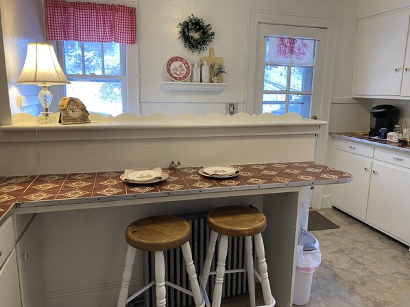 A kitchen with a tiled countertop, two stools, a radiator, and a window with a wreath. - Cape Home In the Beautiful Berkshires - Near Lenox & Bousquet (Pittsfield)