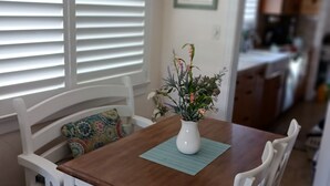 Un comedor con mesa de madera, sillas blancas y un jarrón de flores.