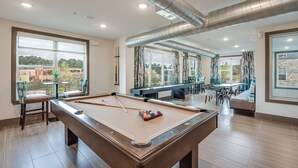 Une table de billard dans une pièce bien éclairée, dotée de grandes fenêtres, un coin salon avec une table de billard et une vue sur l’extérieur.