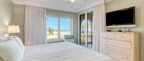 Een slaapkamer met een bed, een plafondventilator, een televisie en uitzicht op het strand.