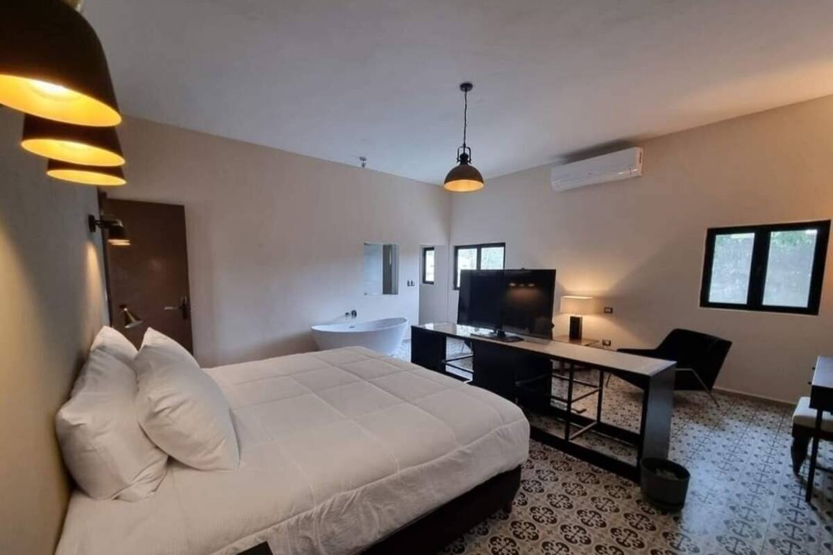 A hotel room with a bed, desk, television, and a window.