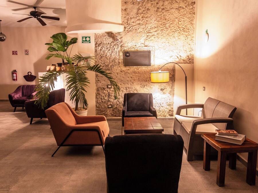 Un salon chaleureux avec un mur d’accent en pierre, un ventilateur de plafond et divers types de sièges, notamment un canapé, des fauteuils et une petite table avec un livre.