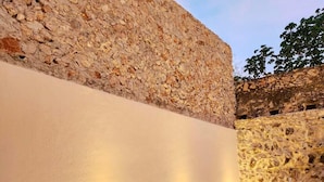 A sunlit outdoor seating area with wicker lounge chairs and a stone wall backdrop. - ACQUA IN BOCCA (Mérida)