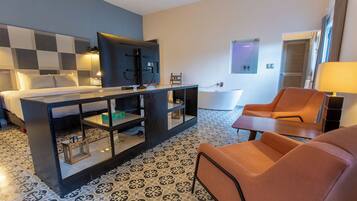 A hotel room with a bed, a TV, a desk with a computer, a chair, a bathtub, and a patterned floor.