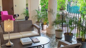 A cozy lounge area with wicker furniture, a table with books, and potted plants.