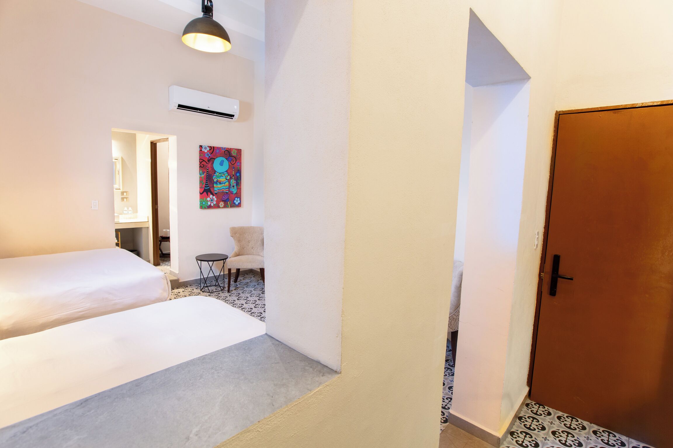 A hotel room with a bed, a chair, a painting, and a door.