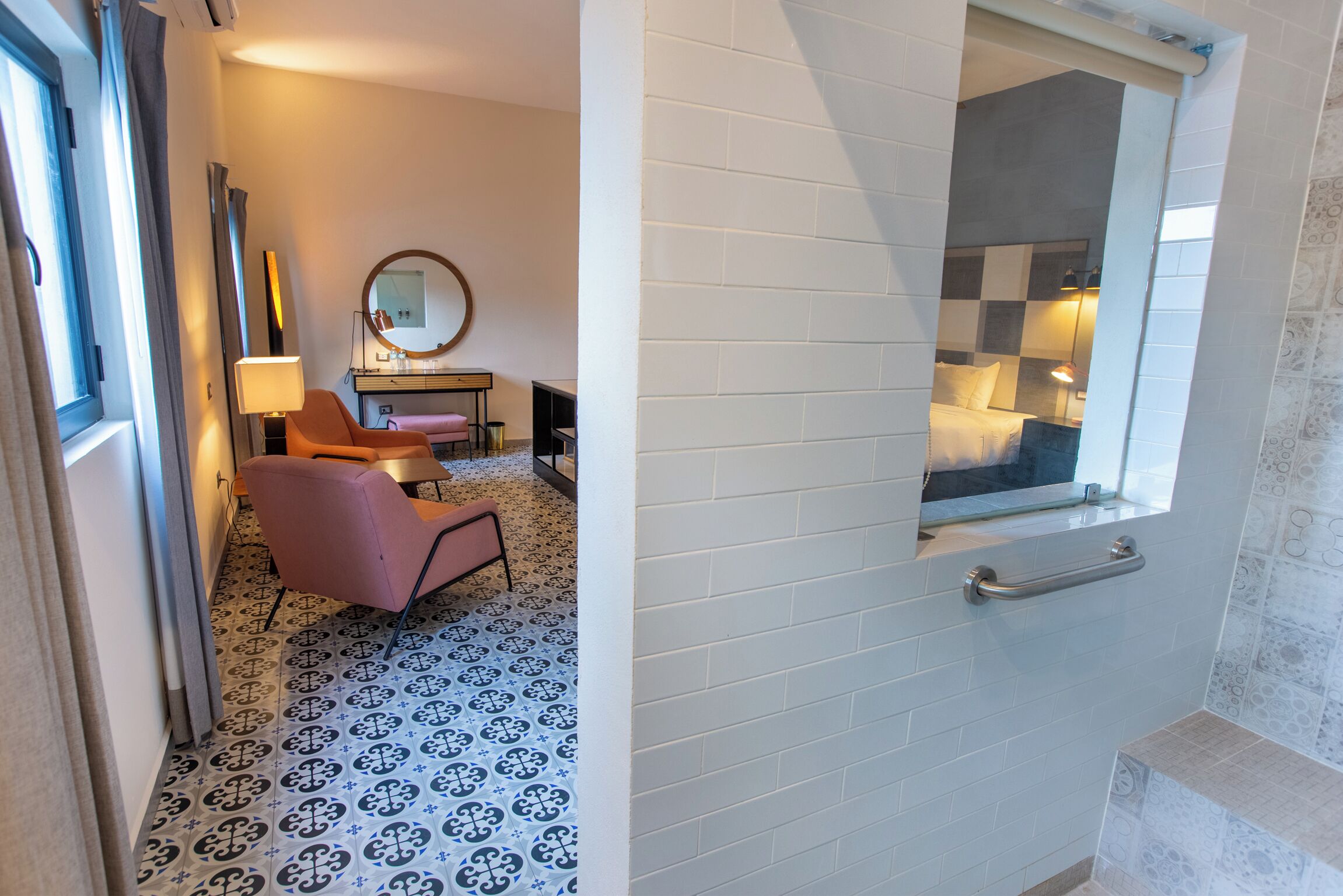 Habitación de hotel con piso a cuadros, cama con cabecera a cuadros, un pequeño escritorio con lámpara y una silla.