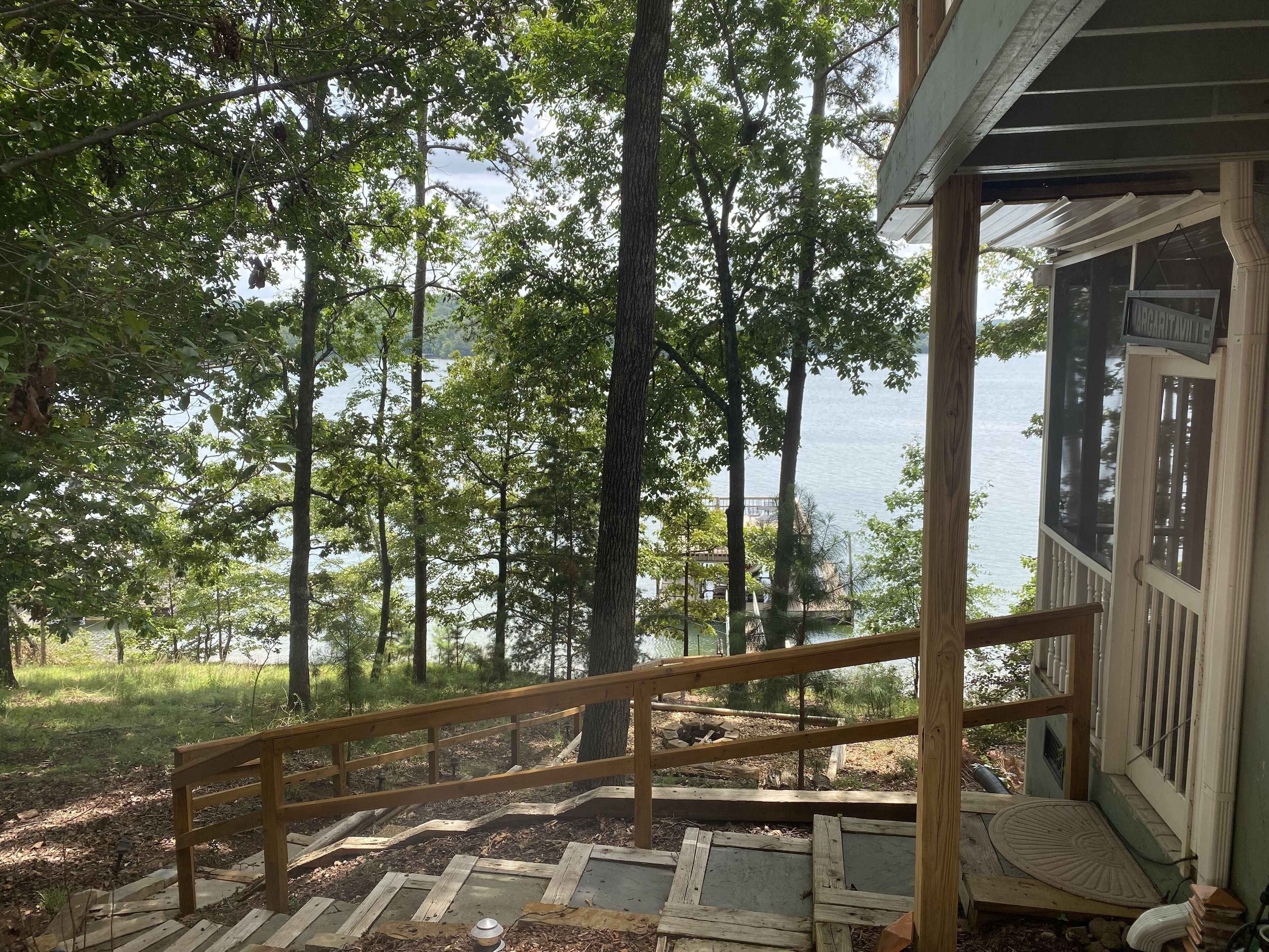 A wooden staircase leading to a porch overlooking a lake, surrounded by trees.