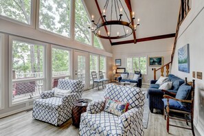 A spacious living room with large windows, a chandelier, and a blue sofa.