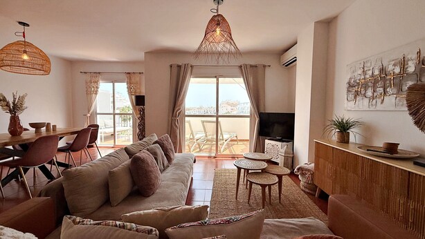 A living room with a sofa, dining table, chairs, a TV, and a balcony with a view. - AP376 VALPARAISO (Nerja)