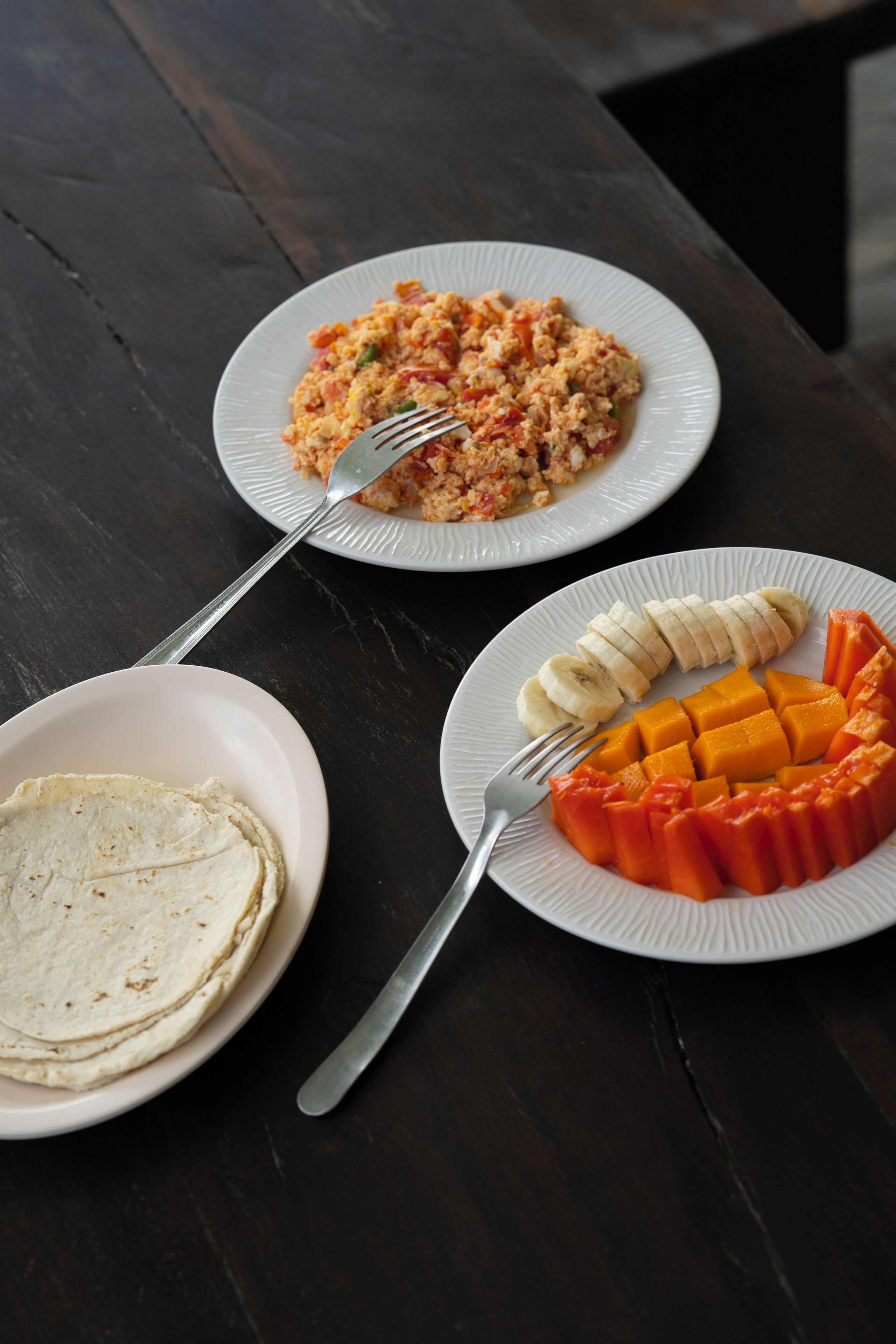 Three plates of food on a dark wooden table.