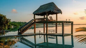 A wooden deck with a thatched roof, a staircase, and lounge chairs by a calm body of water. - Pepos Xul-Ha (Xul-Ha)